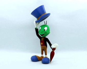 May include: A figurine of a green cricket with a blue top hat, black jacket, and brown pants. The cricket is holding the hat up with a white-gloved hand. It has a red vest, white collar, and a red umbrella.
