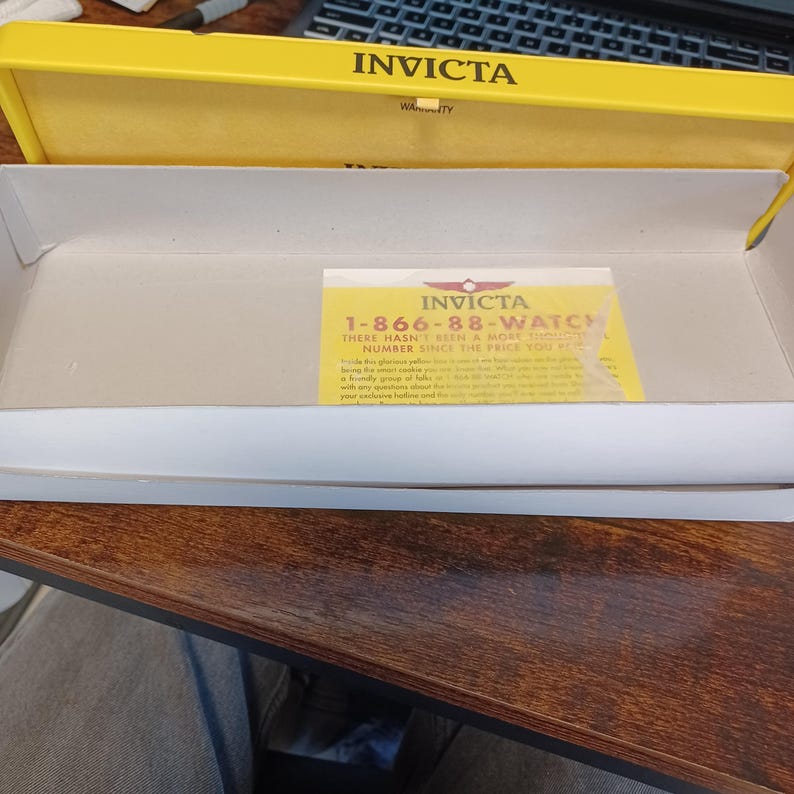May include: An open yellow Invicta watch box with a white interior. A yellow card with the Invicta logo and the phone number 1-866-88-WATCH is inside the box. The Invicta logo and the word "Warranty" are printed on the box.