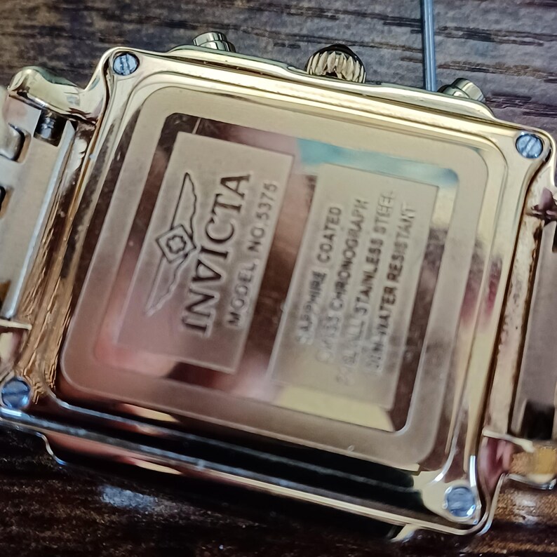 May include: Close-up of a gold-toned Invicta watch. The watch back features the Invicta logo and the text "MODEL NO. 5375". Additional text includes "SAPPHIRE COATED", "SWISS CHRONOGRAPH", "ALL STAINLESS STEEL", and "30M WATER RESISTANT".