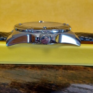 May include: A silver-toned wristwatch with a black leather band. The watch face has a light-colored dial with a rotating bezel. The watch is set against a yellow background.