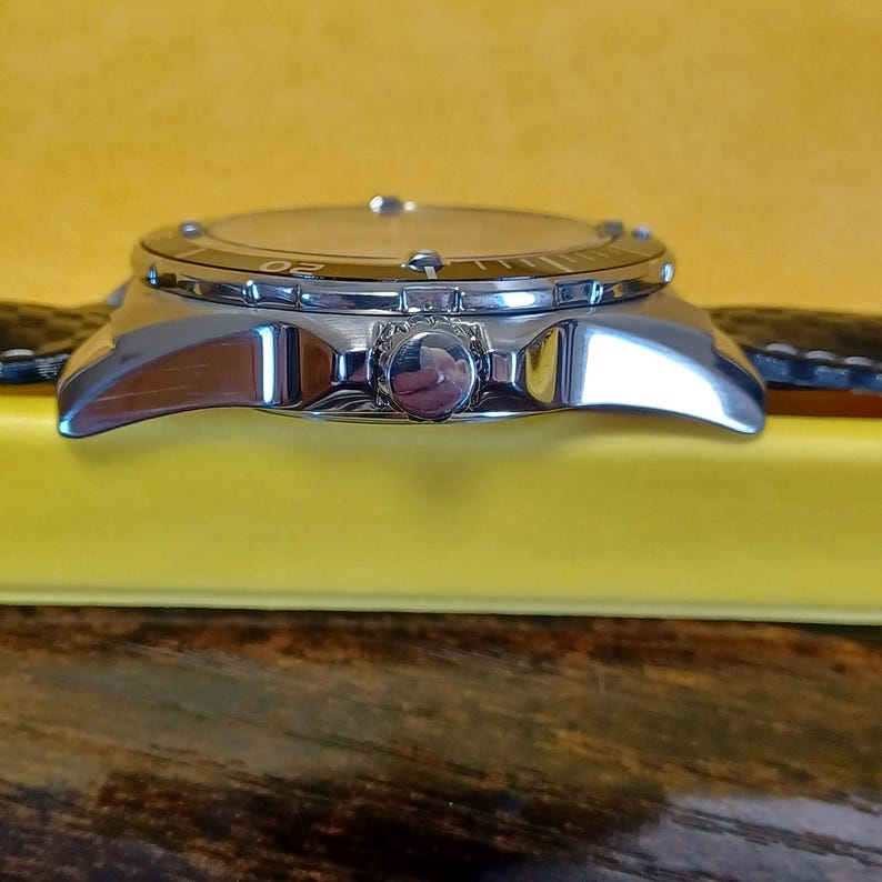 May include: A silver-toned wristwatch with a black leather band. The watch face has a light-colored dial with a rotating bezel. The watch is set against a yellow background.