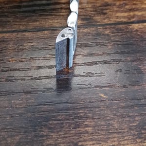 May include: A close-up of a silver metal object with a rectangular shape and a beveled edge. The object is positioned vertically against a dark brown wooden surface, with the light reflecting off the metal.