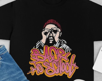 May include: Black t-shirt featuring a graphic of a person wearing glasses and a beanie, with the words "Back to School" in pink and orange graffiti style. Includes blue jeans, a black cap, gold chain, and black trainers.