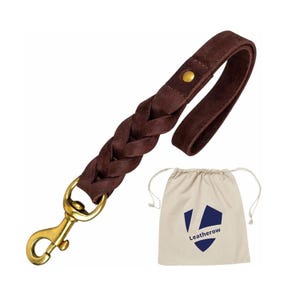 Op de afbeelding: Een donkerbruine leren hondenriem met een gevlochten gedeelte en een goudkleurige sluiting. De riem heeft een lusvormige handgreep en wordt geleverd met een beige trekkoordtas met een blauw logo en de tekst "Leatherow".