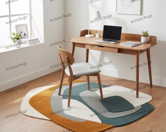 Puede incluir: Una alfombra de área abstracta con una forma y paleta de colores únicos. La alfombra presenta una combinación de blanco, gris, verde azulado y amarillo mostaza. La alfombra está colocada debajo de un escritorio y una silla de madera.