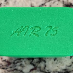 May include: A bright green, rectangular object with rounded edges. The text "A9 R 75" is etched into the surface. The object has a textured appearance and is set against a speckled background.
