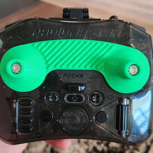 May include: A black and green handheld device with the word "POCKET" printed on it. The device has a green handle and several buttons. The device has the word "SOUND BLASTER" printed on the top.
