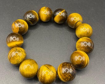 May include: A bracelet made of polished tiger's eye gemstone beads. The beads are round, with a golden-brown color and natural patterns. The bracelet is displayed on a dark gray surface.