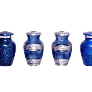 Puede incluir: Cuatro pequeñas urnas azules con detalles plateados. Dos tienen un acabado moteado, las otras un aspecto metálico liso con bandas decorativas. Cada una tiene una tapa a juego.
