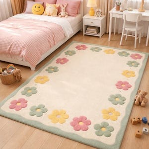 Può includere: Un tappeto rettangolare con sfondo color crema e bordo verde. Presenta un motivo di fiori colorati in rosa, giallo e verde. Il tappeto è posizionato su un pavimento in legno in una camera da letto.
