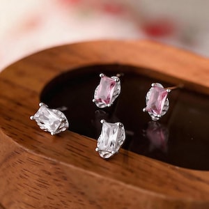 May include: Four stud earrings featuring rectangular-cut stones set in silver-toned metal. Two earrings contain clear white stones, and two earrings contain light pink stones. Each stone is surrounded by a textured, organic-looking metal frame.