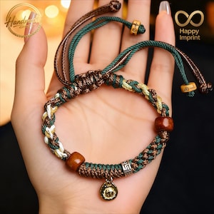 Puede incluir: Pulsera trenzada con hilos marrones, verdes y crema, con cuentas de madera y un pequeño dije dorado. La pulsera ajustable presenta un diseño de macramé.