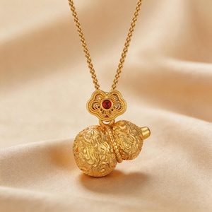 Handmade 18K gold plated filigree gourd pendant necklace featuring matte finish surface. Classic double-bulb Hulu shape with intricate cloud scroll openwork patterns. Stylized four-lobed flower bail with vibrant red gemstone center accent. Twisted rope chain, nickel-free copper alloy. 50cm length, 10g weight. Lucky charm symbolizing health and prosperity.