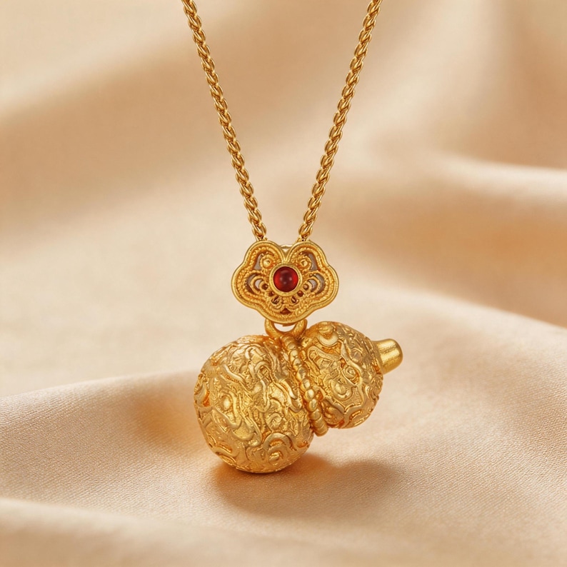 Handmade 18K gold plated filigree gourd pendant necklace featuring matte finish surface. Classic double-bulb Hulu shape with intricate cloud scroll openwork patterns. Stylized four-lobed flower bail with vibrant red gemstone center accent. Twisted rope chain, nickel-free copper alloy. 50cm length, 10g weight. Lucky charm symbolizing health and prosperity.