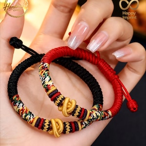 Può includere: Due braccialetti fatti a mano, uno nero e uno rosso. Entrambi presentano un motivo intrecciato colorato con dettagli dorati. I braccialetti sono tenuti in una mano. L'immagine include il testo "Handmade" e "Happy Imprint".