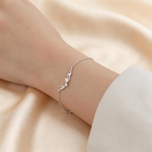 May include: A delicate silver bracelet featuring a floral design with small, sparkling accents. The bracelet is worn on a wrist, showcasing its intricate details and elegant style. The chain is thin and the bracelet appears to be made of sterling silver.