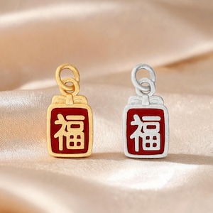 May include: Two rectangular charms with a matte finish, one in gold tone and one in silver tone. Each charm features a red enamel center with the Chinese character for good fortune, topped with a small bow detail and a circular jump ring.