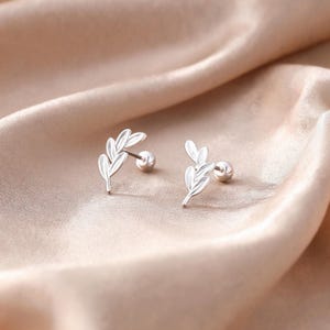 May include: A pair of silver-toned stud earrings featuring a delicate leaf branch design. Each earring consists of a curved stem with multiple small, smooth leaves and a round ball backing, providing a secure fit for the wearer's earlobe.