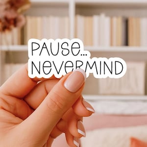 May include: A white die-cut vinyl sticker with a black outline and black sans-serif text that reads PAUSE... NEVERMIND. The sticker features a smooth, matte finish and is shaped to follow the contours of the bold, rounded lettering.