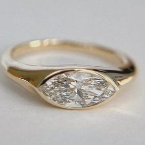 May include: A gold ring featuring a marquise-cut diamond. The diamond is set within a bezel, and the band is smooth and polished. The ring is a classic and elegant piece of jewellery.