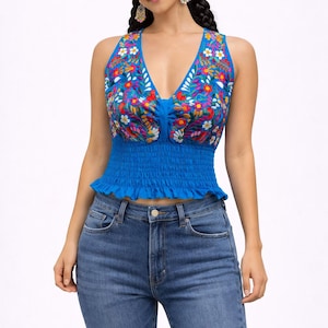 May include: A bright blue halter top with a V-neck, decorated with colourful floral embroidery. The top has a smocked waist and a ruffled hem. Worn with blue denim jeans.