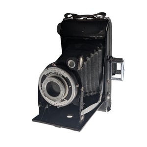 Könnte beinhalten: Eine schwarze Vintage-Faltkamera mit Balgenmechanismus. Die Objektiveinheit verfügt über eine silberne kreisförmige Platte mit dem Text Lumirex, Anastigmat und Fidor. Sie enthält einen Metallsucher an der Seite und eine klappbare Frontplatte.