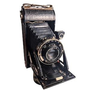 May include: A vintage Voigtländer Bessa folding camera in black with a leather-covered body and a black bellows. The lens assembly features the text Anastigmat Voigtar 1:6.3 F=10.5 cm Voigtländer Braunschweig, with shutter speed settings.