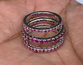 Peut inclure: Trois bagues en argent empilées, chacune ornée d'une rangée continue de petites pierres précieuses roses vibrantes. Les bagues sont présentées sur un fond neutre, mettant en valeur leur design et leur couleur.