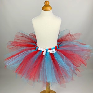 May include: A red and blue tulle tutu with a white ribbon and a striped blue and red waistband.