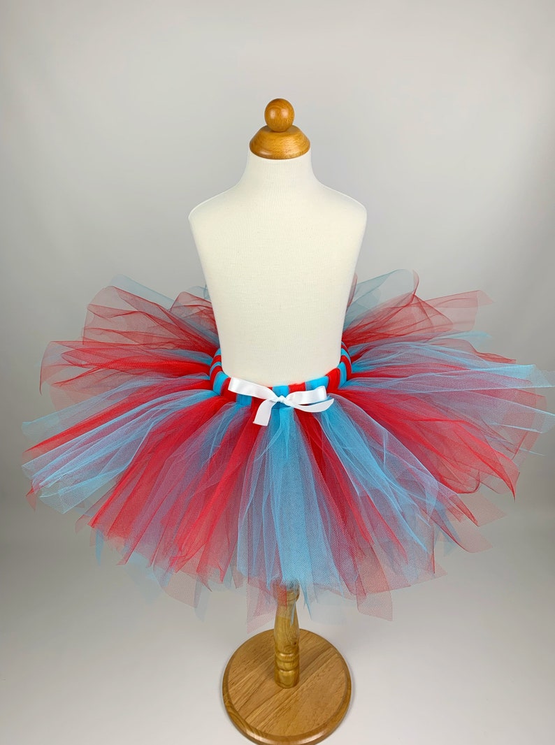 May include: A red and blue tulle tutu with a white ribbon and a striped blue and red waistband.