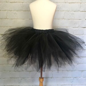 May include: A black tulle tutu skirt on a white mannequin. The skirt is full and fluffy, with multiple layers of tulle.