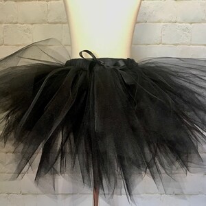 May include: A black tulle tutu skirt with a satin ribbon tie. The skirt is full and fluffy, perfect for a dance recital or costume.