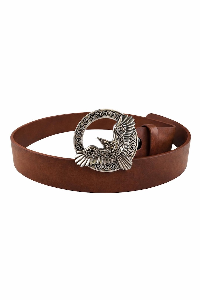 May include: A brown leather belt with a silver-colored buckle. The buckle features a detailed design of a bird within a circular frame. The belt is a medium brown color and appears to be made of genuine leather.
