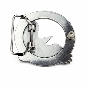 May include: A silver-colored metal belt buckle with a bird design. The buckle has a circular frame with a bird silhouette in the center. The buckle has a rectangular bar and a pin for securing the belt.