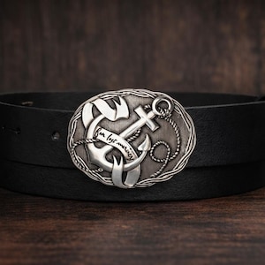 May include: Black leather belt with a silver-colored oval buckle featuring an anchor design. The buckle has the words "for lost mariners" engraved on it. The belt is displayed on a dark wooden surface.