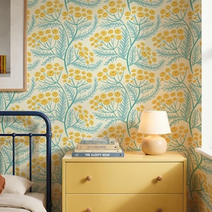 Blue and yellow cottagecore wildflower wallpaper. The flowers are hand drawn in a folk art botanical style on a cream background. Styled in a bedroom with a yellow dresser, a blue metal headboard, and a framed picture on the wall.