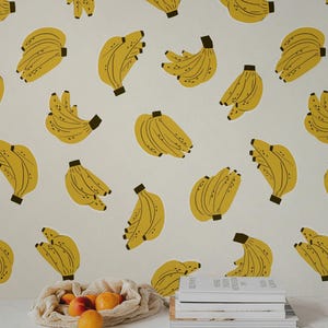 Könnte beinhalten: Ein sich wiederholendes Muster aus gelben Bananen auf weißem Hintergrund. Vor einem Stapel Bücher liegt ein Netzbeutel mit Orangen und Pfirsichen. Die Bananen haben schwarze Stiele und sind verstreut.