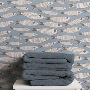 May include: A stack of three folded dark blue towels resting on a white stool against a light blue wallpaper background featuring a repeating pattern of beige fish with dark brown fins and outlines, arranged in a horizontal swimming orientation.