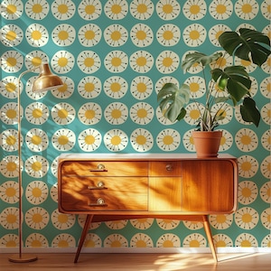 May include: A wooden sideboard with three drawers and a cabinet door stands against a teal wallpaper featuring a repeating pattern of yellow circles with radiating lines. A tall floor lamp and a potted plant sit beside the wooden furniture.