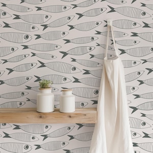 May include: A light-colored wall with a repeating pattern of dark gray line-drawn fish. A natural wood shelf holds two white ceramic canisters with wooden lids. A plain white apron hangs from a hook on the right side of the wall.