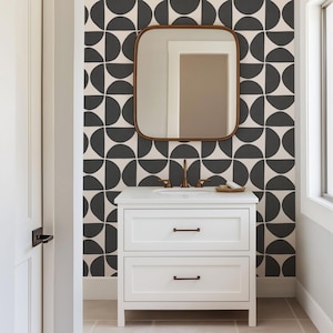 Peut inclure: Un meuble-lavabo blanc à deux tiroirs avec des poignées en bronze, placé contre un mur au motif géométrique répétitif de demi-cercles gris foncé sur fond crème, surmonté d'un miroir carré aux coins arrondis.