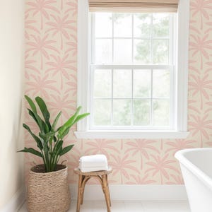 Puede incluir: Papel pintado con un patr&oacute;n repetitivo de palmeras rosas sobre un fondo crema. El papel est&aacute; instalado en una pared con un marco de ventana blanco, una persiana tejida, una planta verde en una cesta y un peque&ntilde;o taburete de madera.