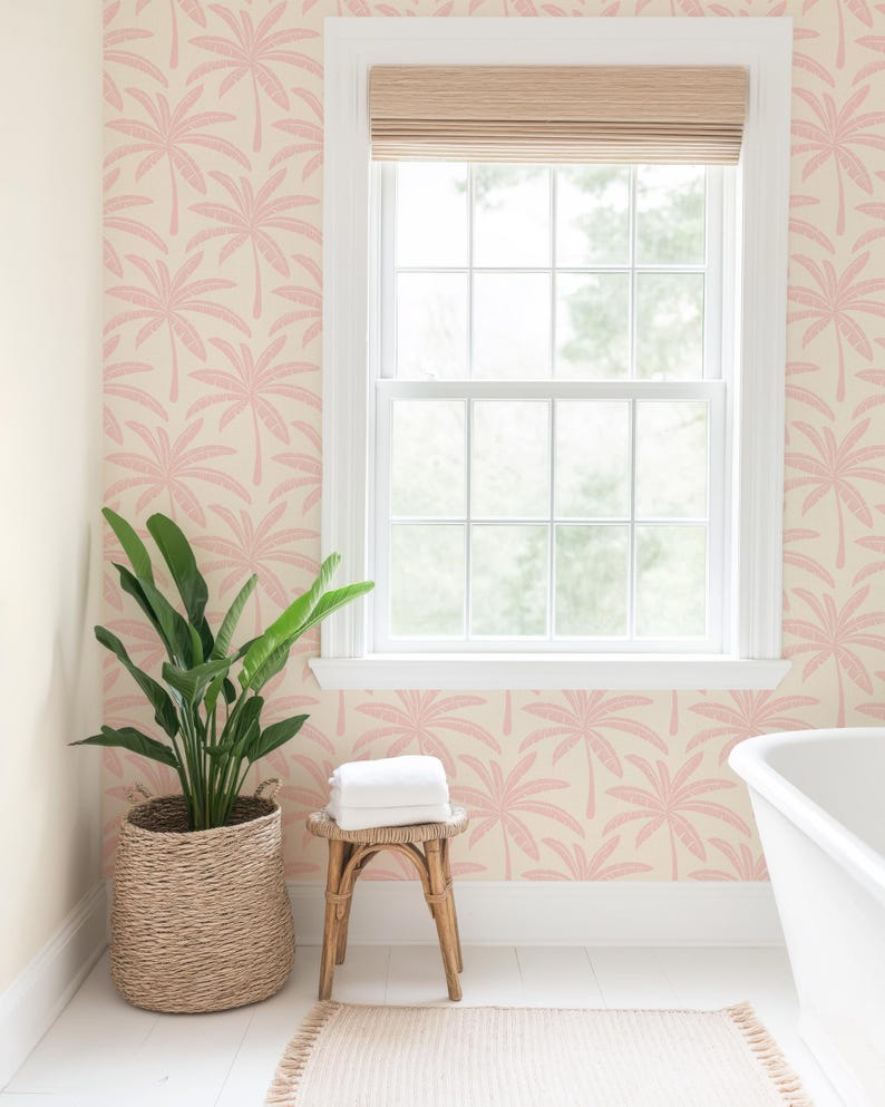 Puede incluir: Papel pintado con un patr&oacute;n repetitivo de palmeras rosas sobre un fondo crema. El papel est&aacute; instalado en una pared con un marco de ventana blanco, una persiana tejida, una planta verde en una cesta y un peque&ntilde;o taburete de madera.