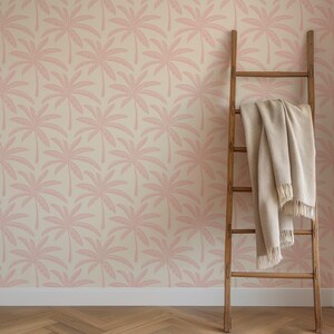 Puede incluir: Una escalera de madera apoyada contra una pared con papel pintado que presenta un patr&oacute;n repetitivo de siluetas de palmeras rosas sobre un fondo crema. Una manta tejida de color beige con flecos cuelga de los pelda&ntilde;os de la escalera.