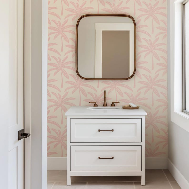 Puede incluir: Un mueble de ba&ntilde;o blanco con dos cajones y herrajes de metal oscuro, con un lavabo y grifo blancos. Sobre el mueble cuelga un espejo rectangular de esquinas redondeadas frente a un papel tapiz con un patr&oacute;n repetido de palmeras rosas.