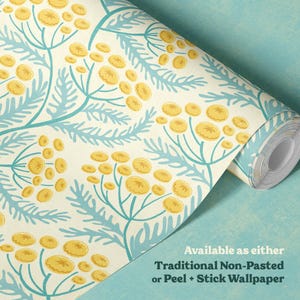 Wallpaper roll with a blue and yellow wildflower floral print on a cream background in a cottagecore style lies unrolled on a textured turquoise surface.  The text reads that the wallpaper design is available as traditional non-pasted or peel and stick wallpaper