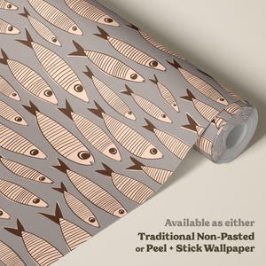 Pode incluir: Um rolo de papel de parede com um padrão repetitivo de peixes rosa claro com barbatanas e contornos castanho-escuros sobre um fundo cinzento sólido. O texto na imagem diz: Available as either Traditional Non-Pasted or Peel + Stick Wallpaper.