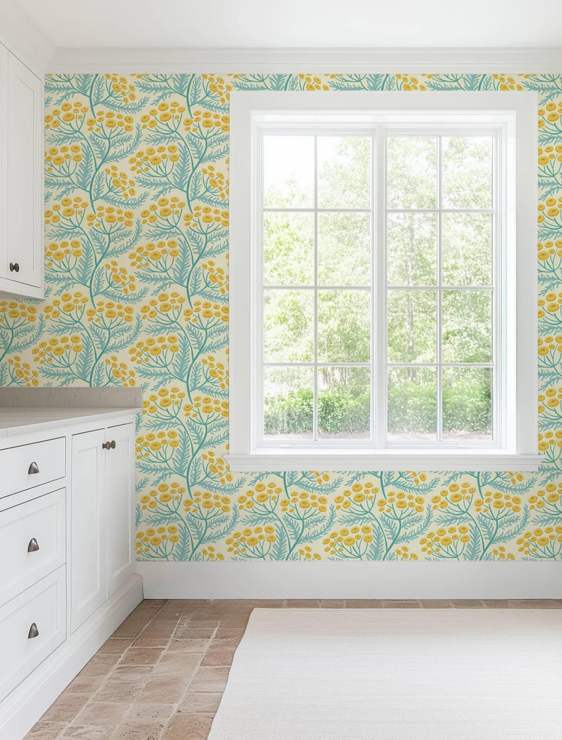 a bright and airy kitchen with a large window that provides a view of the outdoors. The walls are adorned with a vibrant floral wallpaper pattern in shades of yellow and green, creating a cheerful and lively atmosphere. The kitchen features white cabinets and drawers, complementing the overall color scheme of the room.
