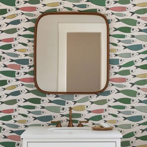 May include: A square mirror with rounded corners and a thin bronze frame mounted on a wall covered in wallpaper featuring a repeating pattern of stylized fish in shades of green, blue, yellow, and pink, positioned above a white bathroom vanity.