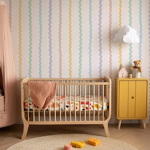 Pode incluir: Um berço de madeira com um lençol estampado de formas vermelhas, laranjas e azuis, coberto por uma manta cor de pêssego. Ao lado, um armário amarelo com um urso de peluche e um candeeiro de parede em forma de nuvem sobre papel de parede.